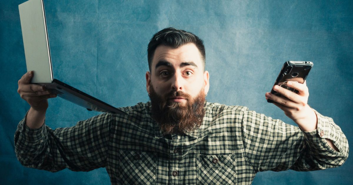 フリーWiFiの危険性に不安を感じる、ノートPCとスマートフォンを持つ男性の様子